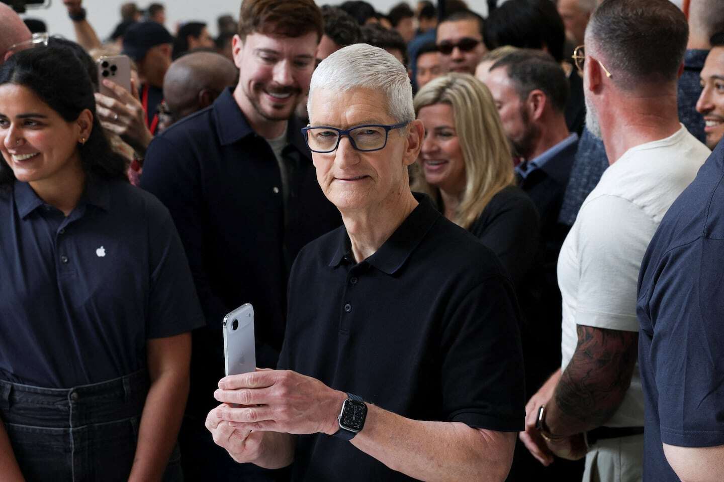 Tim Cook, CEO de Apple, sostiene un iPhone mientras se encuentra en un evento con un grupo de personas