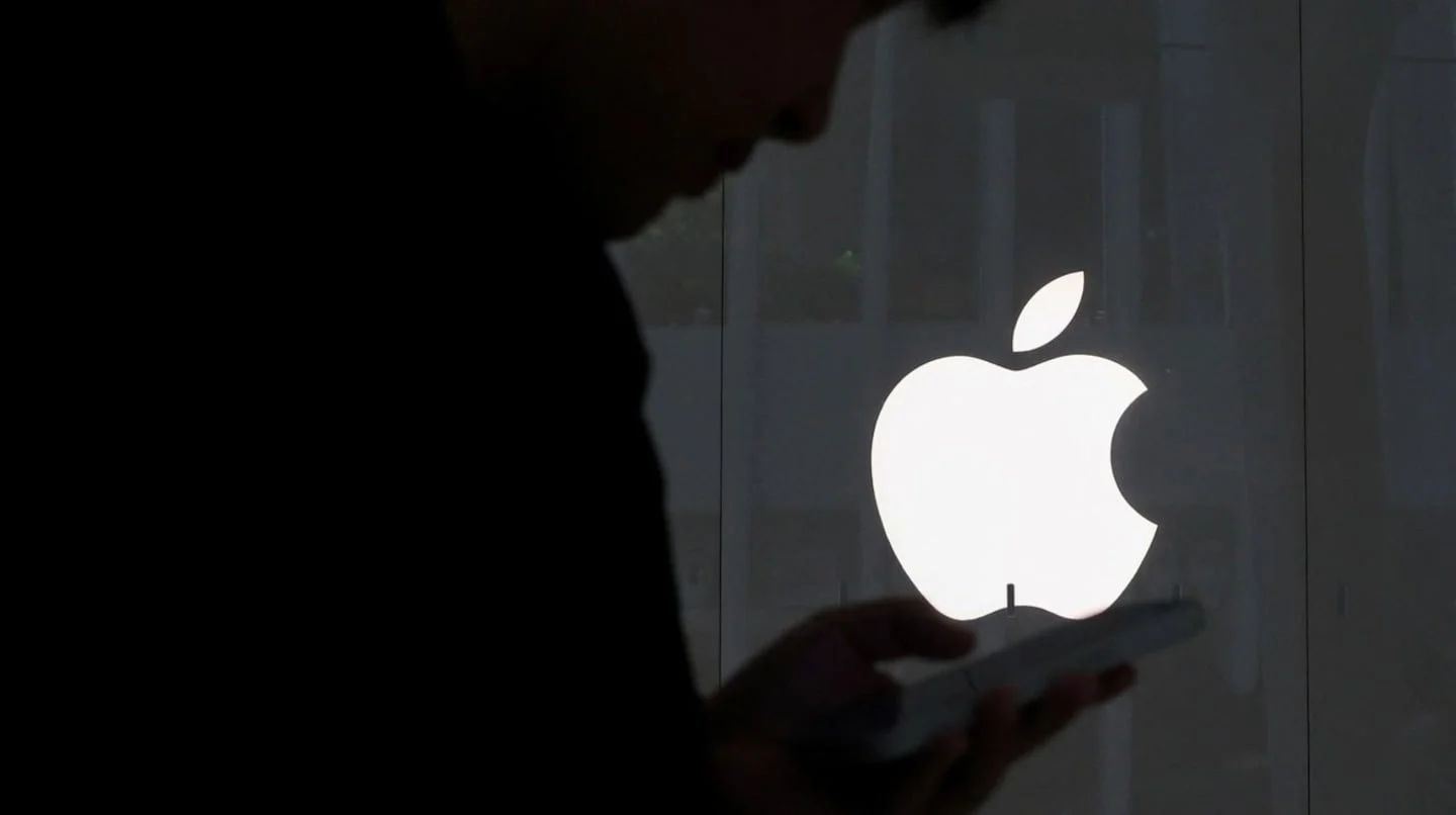 Silueta de una persona usando un smartphone frente al logo de Apple
