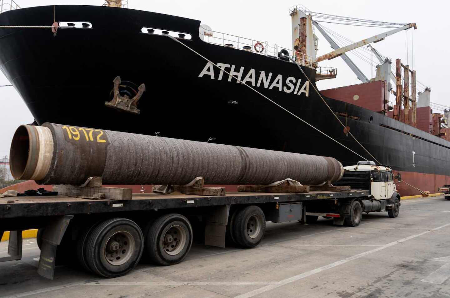 Camión con tubería de petróleo frente al buque de carga Athanasia en puerto
