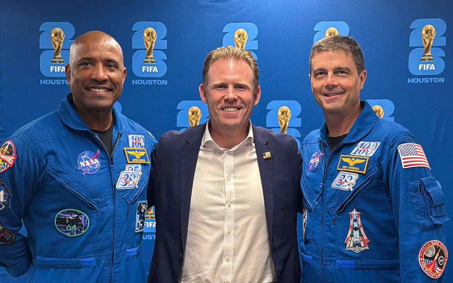 Tres hombres en trajes de astronauta posan frente a un fondo con el logo de la FIFA y la Copa del Mundo