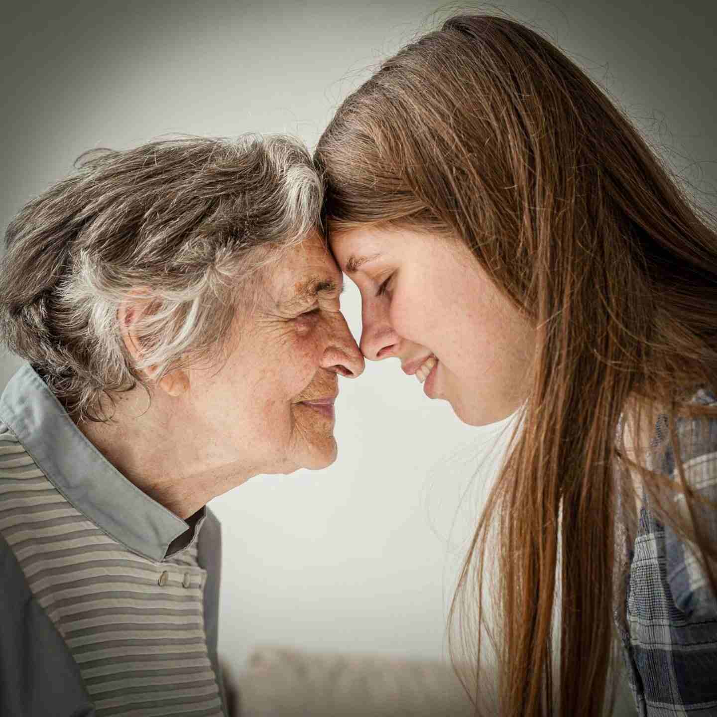 Una mujer joven sonríe mientras toca la frente de una anciana en un ambiente acogedor
