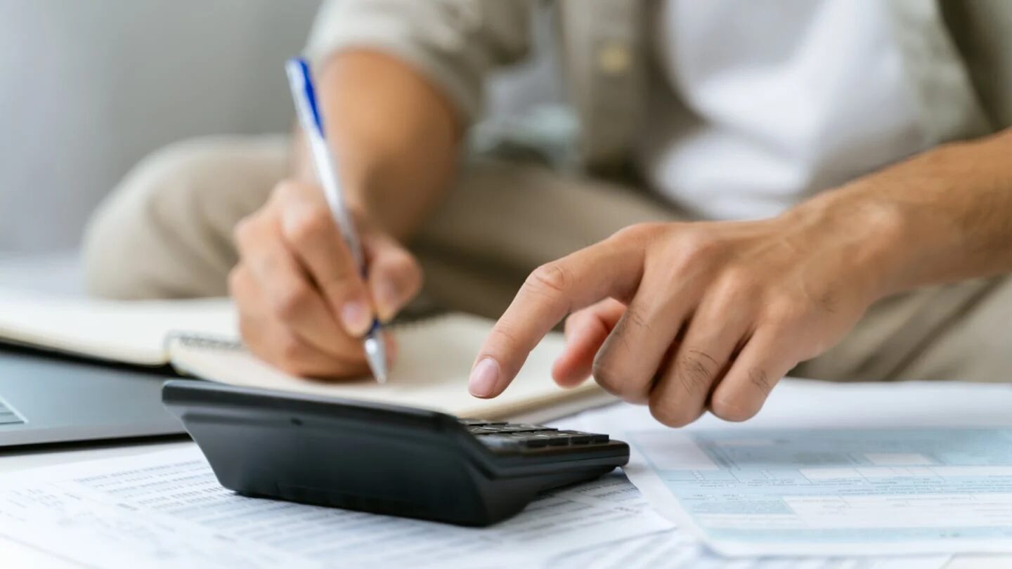 Persona calculando impuestos con calculadora y cuaderno