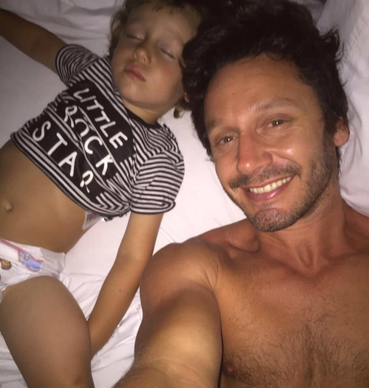 Benjamín Vicuña sonríe junto a su hijo mientras ambos descansan en la cama