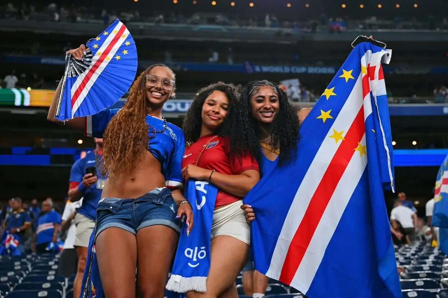 Tres mujeres celebrando con banderas de Cabo Verde en un estadio