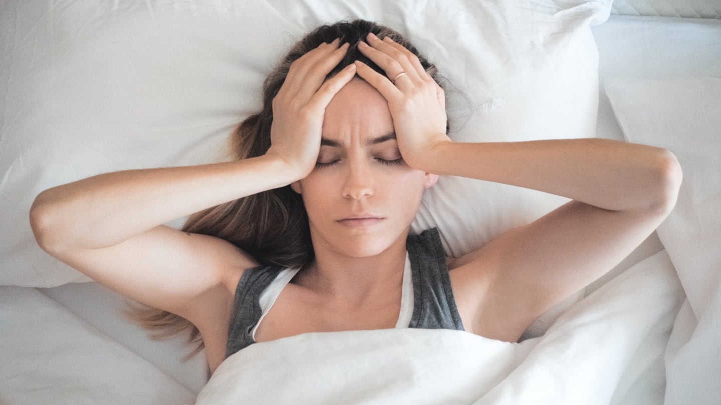 Mujer con dolor de cabeza en la cama, sosteniendo su cabeza con las manos