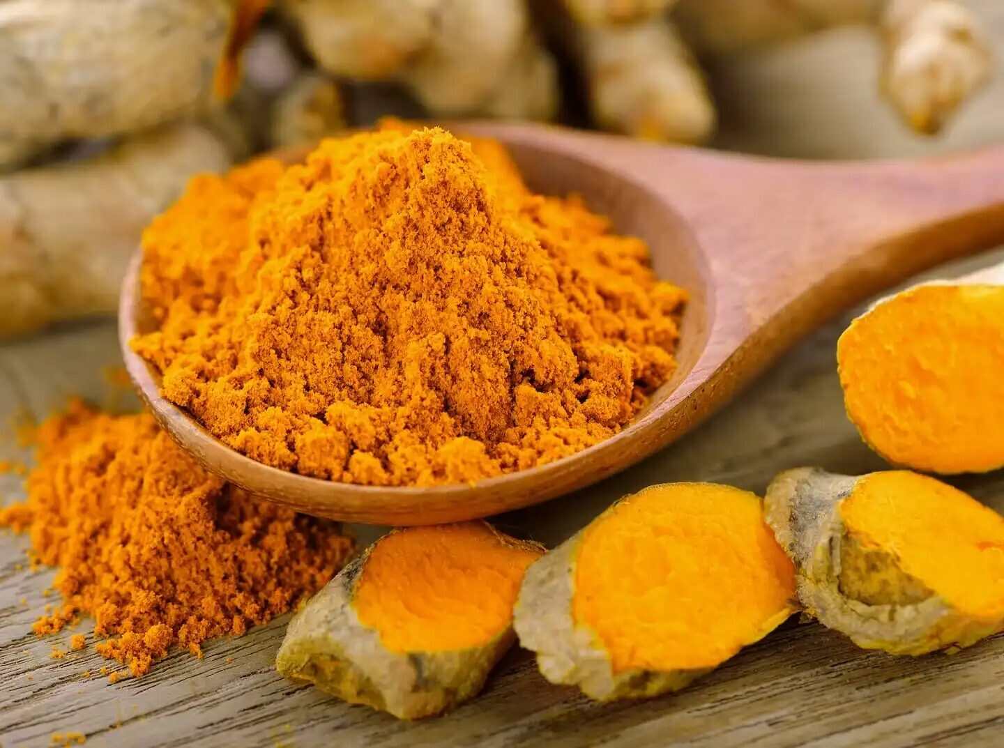 Cúrcuma en polvo y raíz de cúrcuma fresca sobre una cuchara de madera