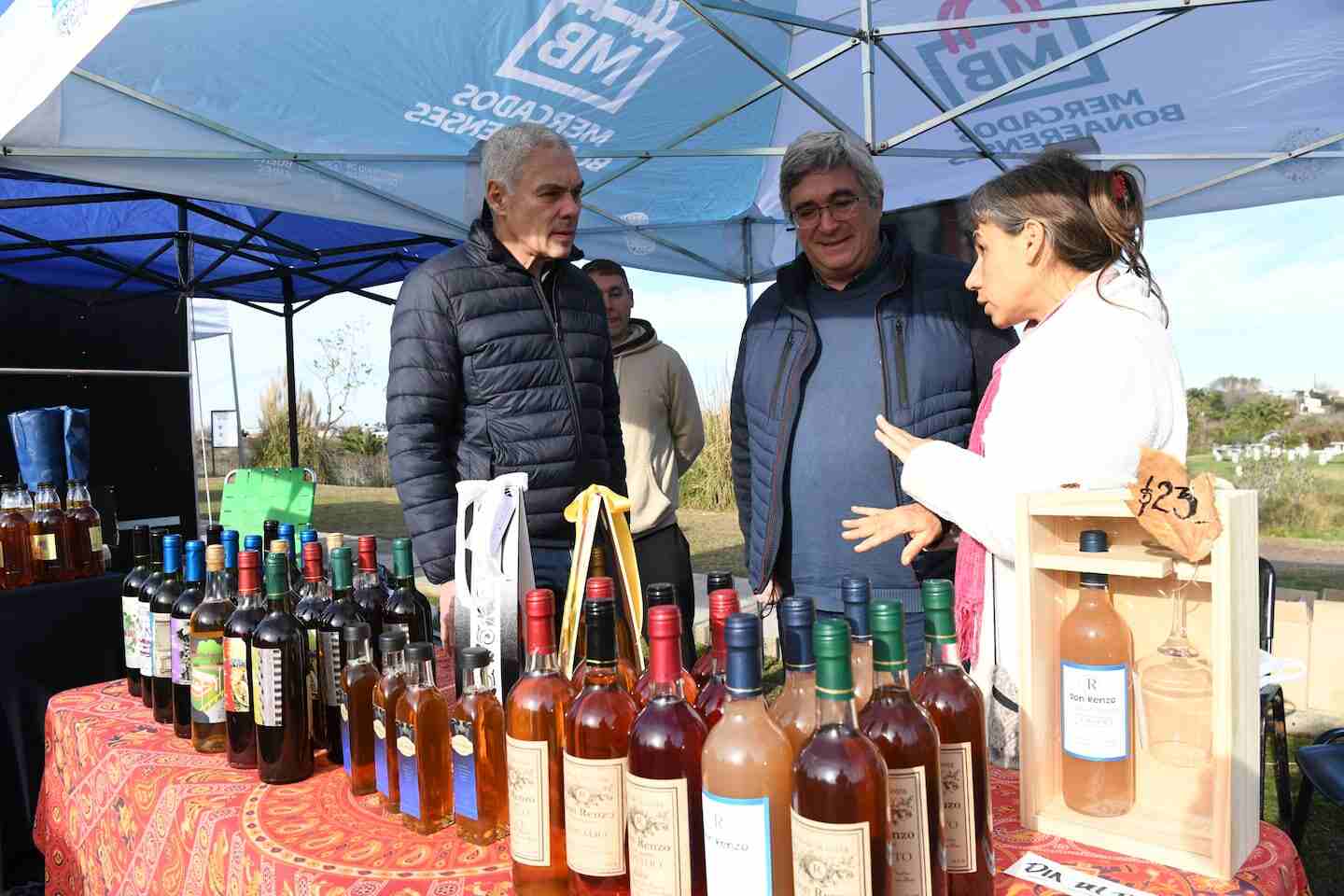 Tres personas conversando frente a una mesa con botellas de miel en un evento apícola en Buenos Aires