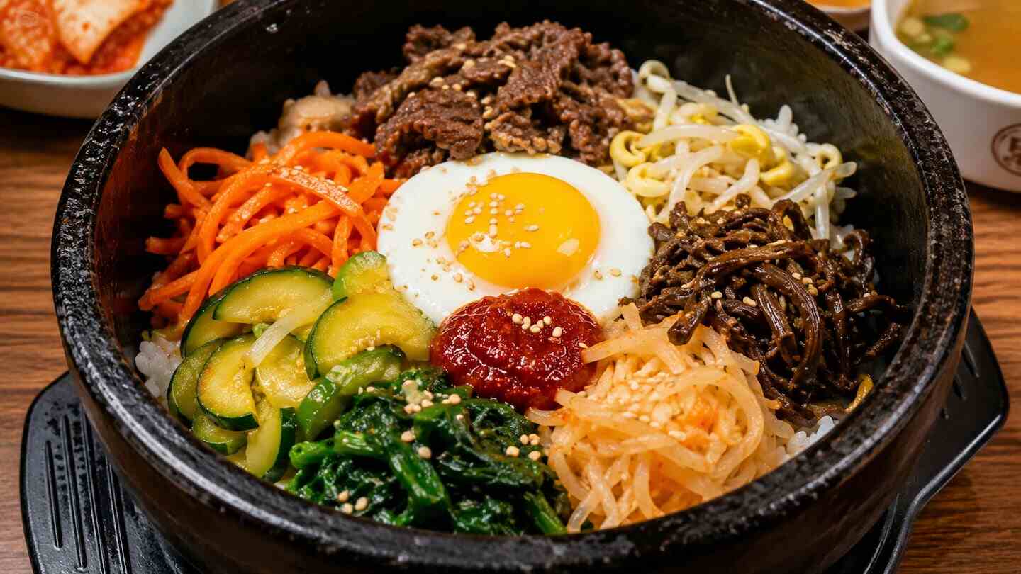 Plato de bibimbap servido en un tazón de piedra con arroz, verduras, carne y huevo