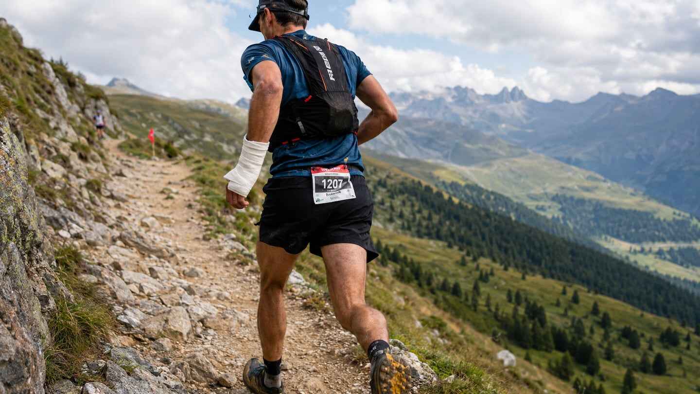 Corredor con vendaje en el brazo participando en una carrera de montaña en un paisaje montañoso