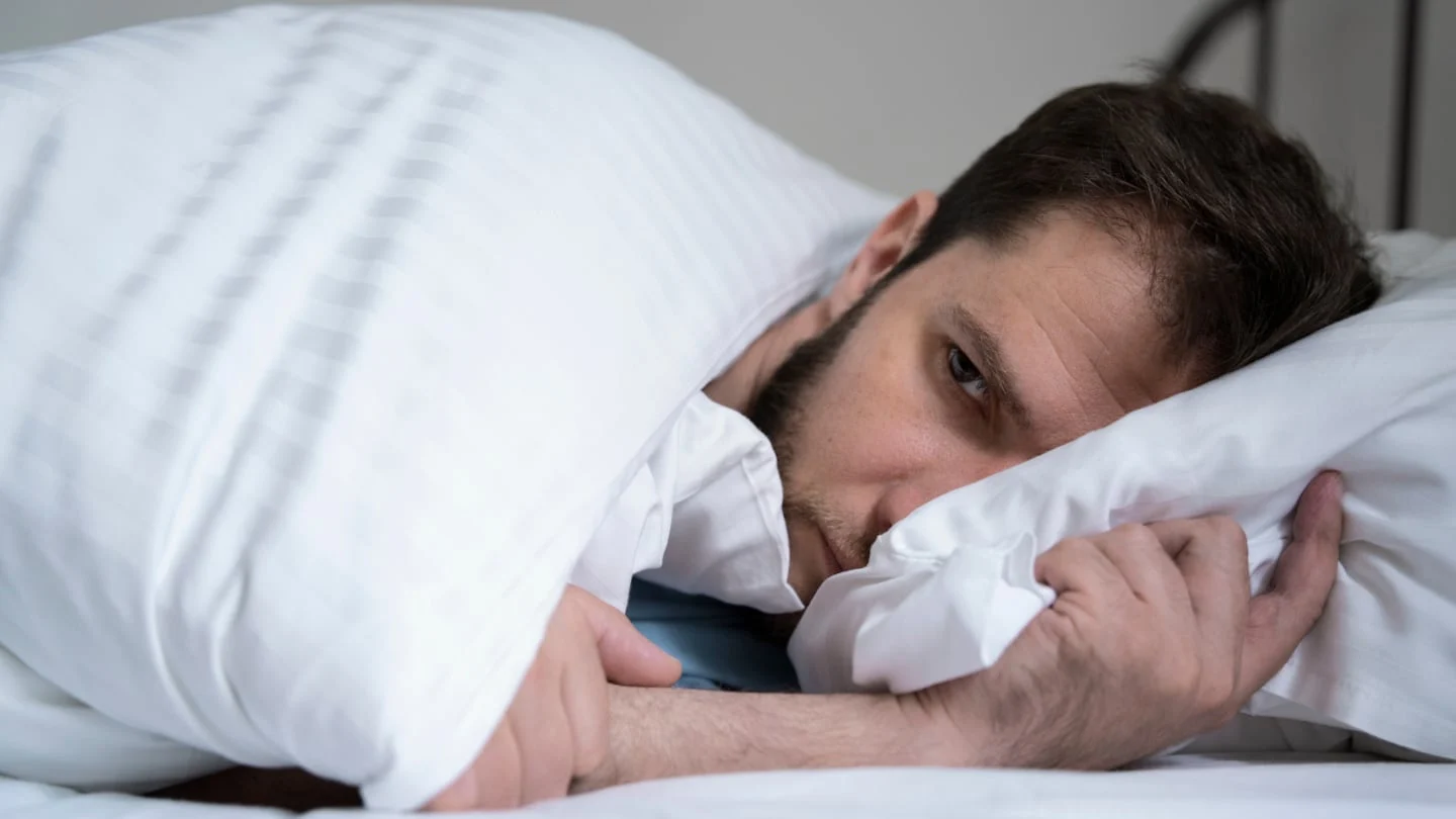 Hombre despertando en la cama con expresión preocupada