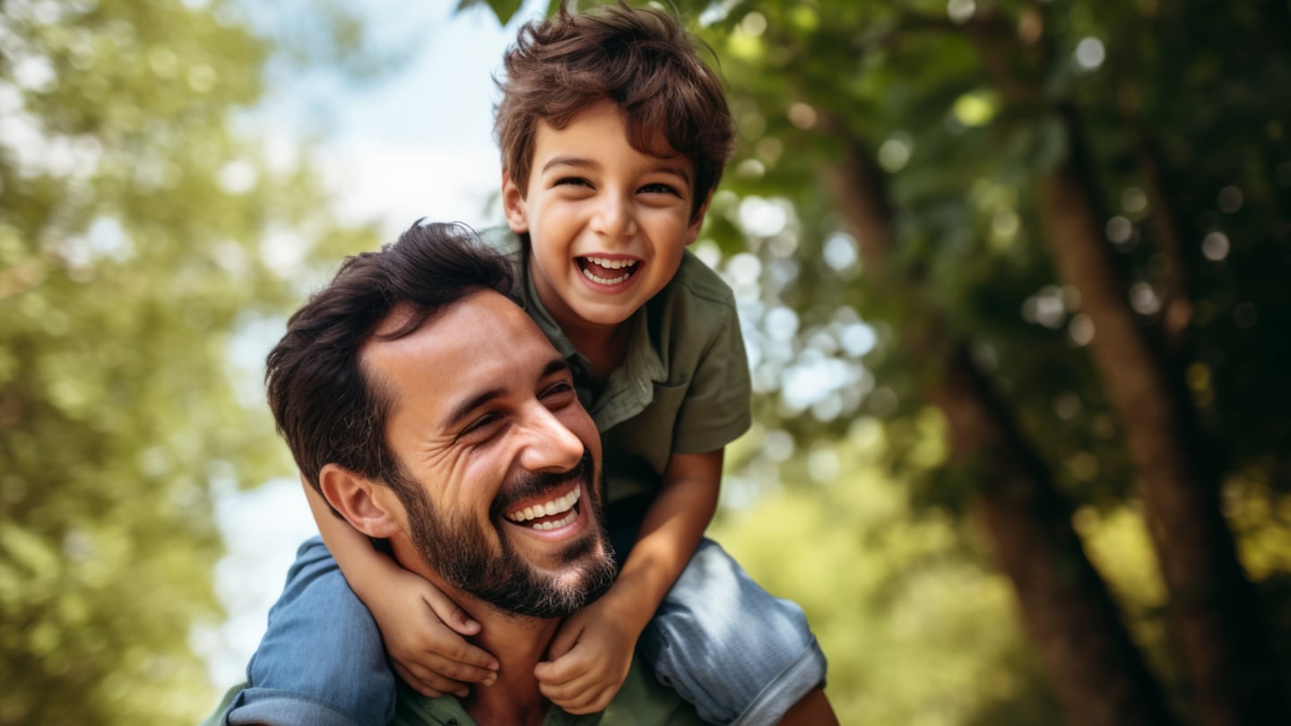 Padre sonriente cargando a su hijo en la espalda en un entorno natural