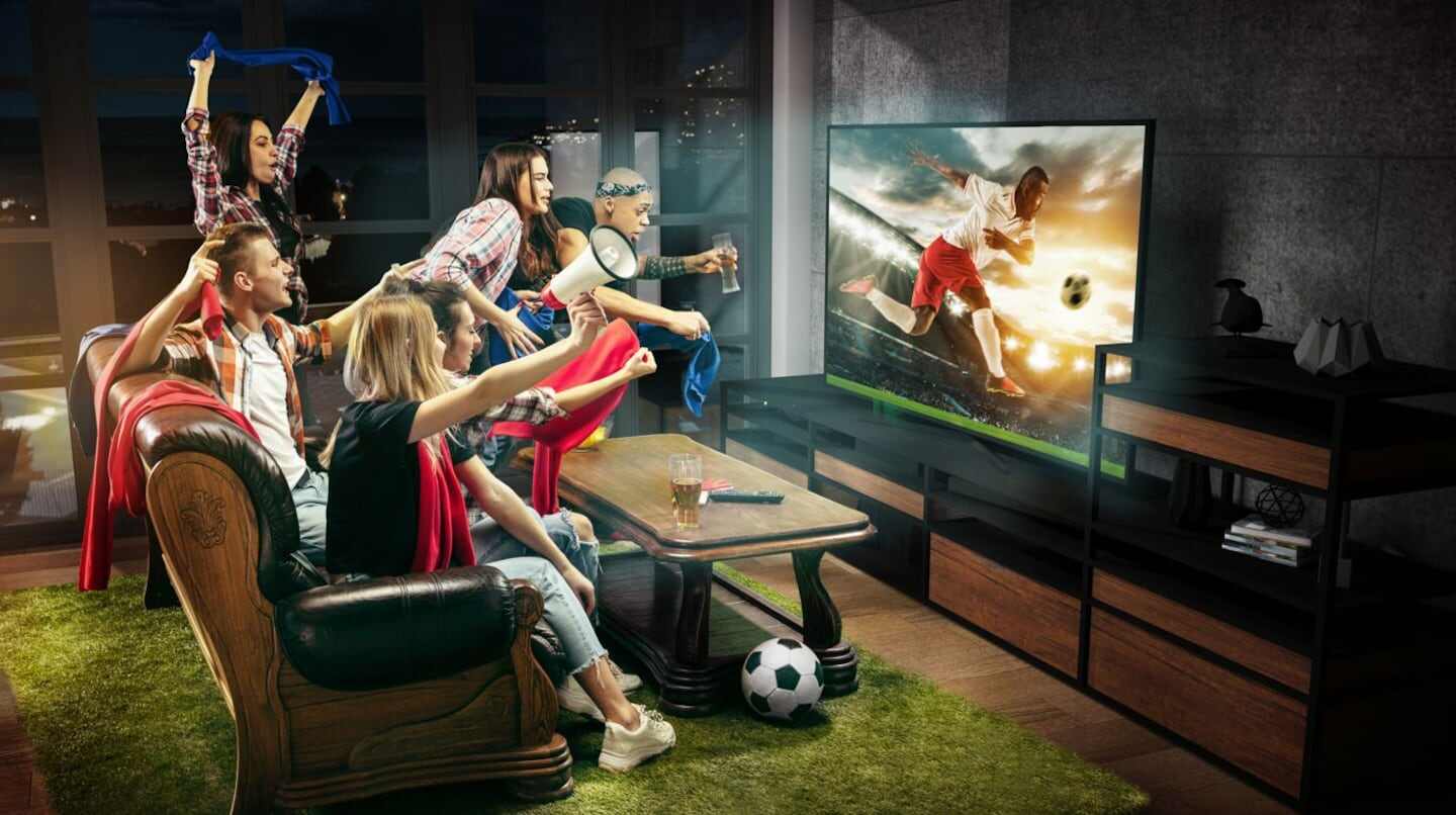 Grupo de personas animadas viendo un partido de fútbol en televisión
