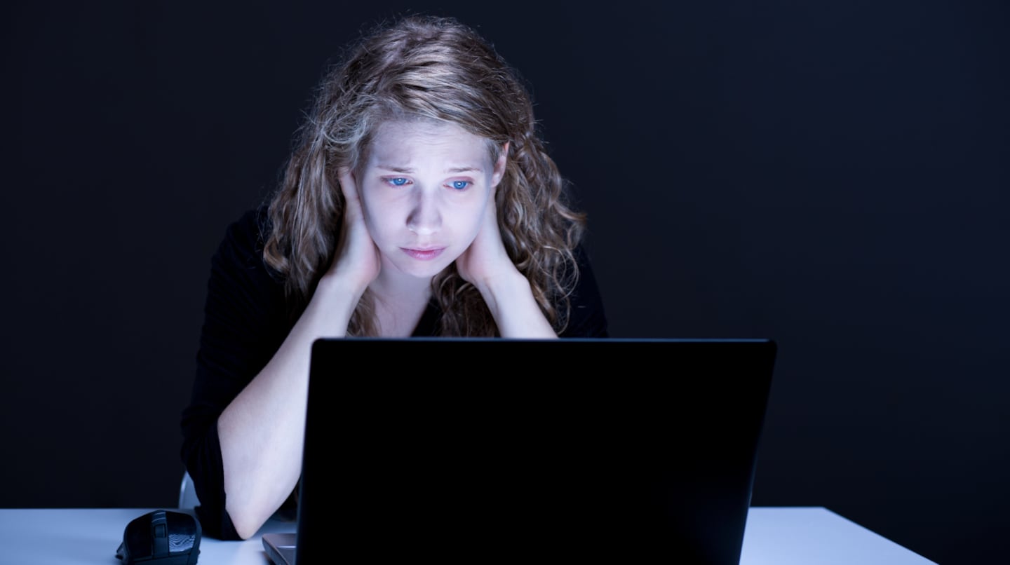 Mujer con expresión de preocupación frente a una computadora portátil en un entorno oscuro
