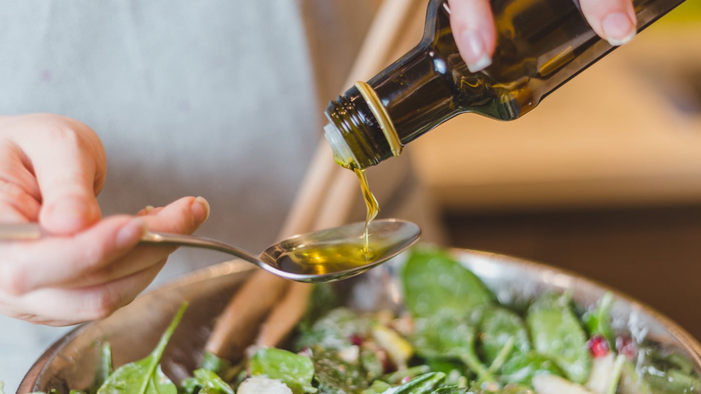 Persona vertiendo aceite de oliva en una cuchara sobre una ensalada fresca
