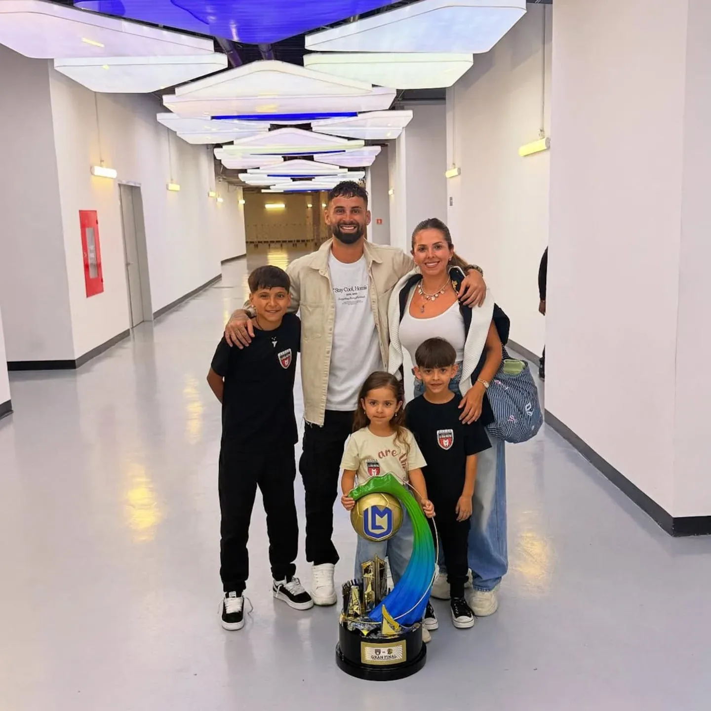 Lucas Trejo posando con su familia y un trofeo en un pasillo iluminado