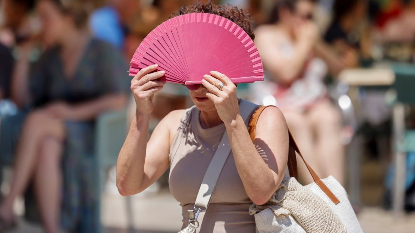 Mujer usando un abanico para protegerse del calor extremo en un día soleado