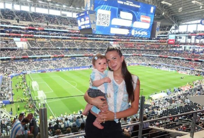 Ailén Cova sosteniendo a su bebé en un estadio de fútbol con el campo de juego visible