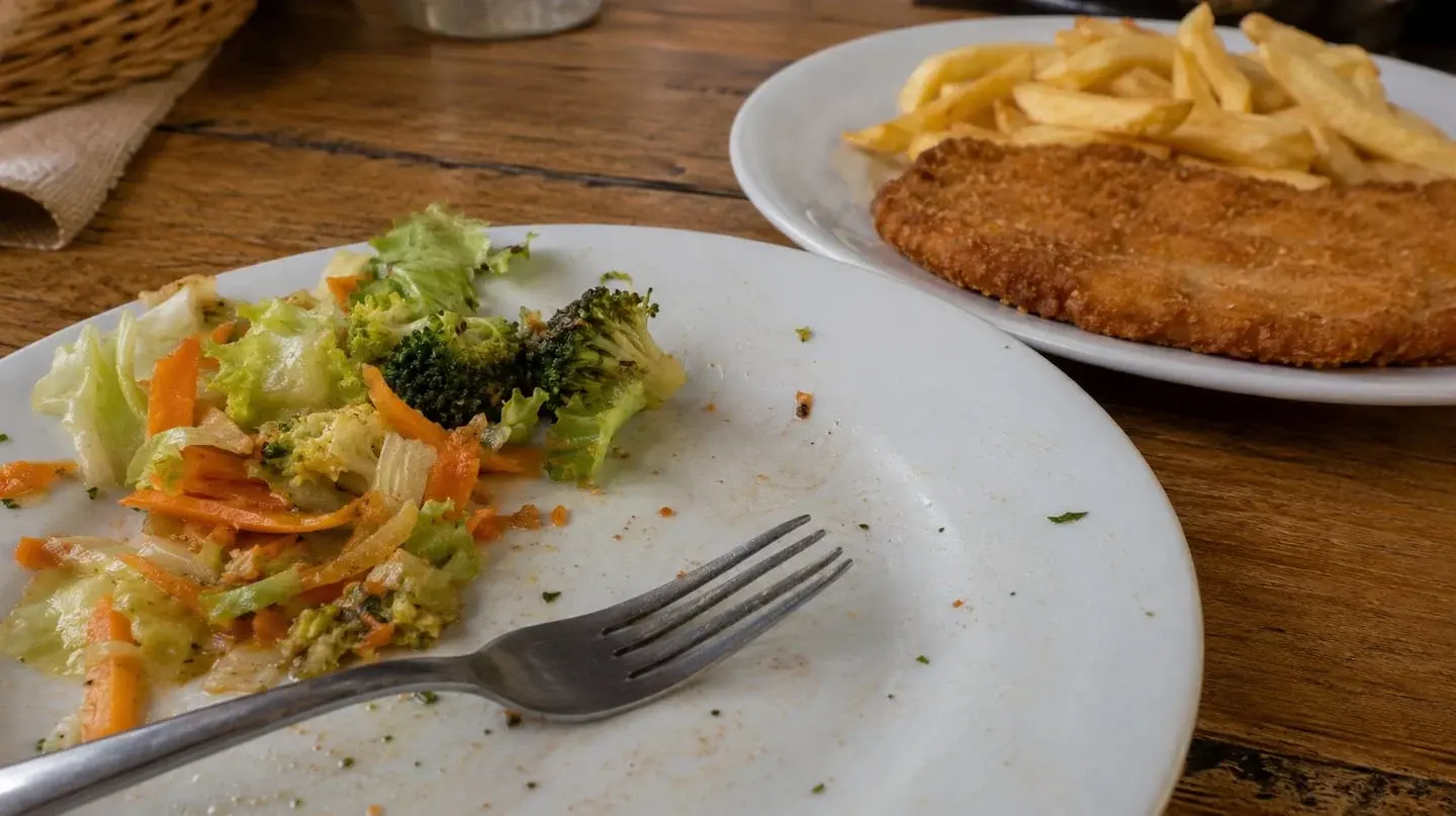 Plato con restos de ensalada y un plato de papas fritas y carne al fondo