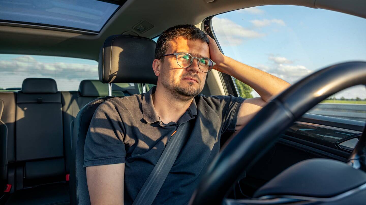 Hombre con gafas sentado al volante de un coche, mostrando preocupación mientras conduce