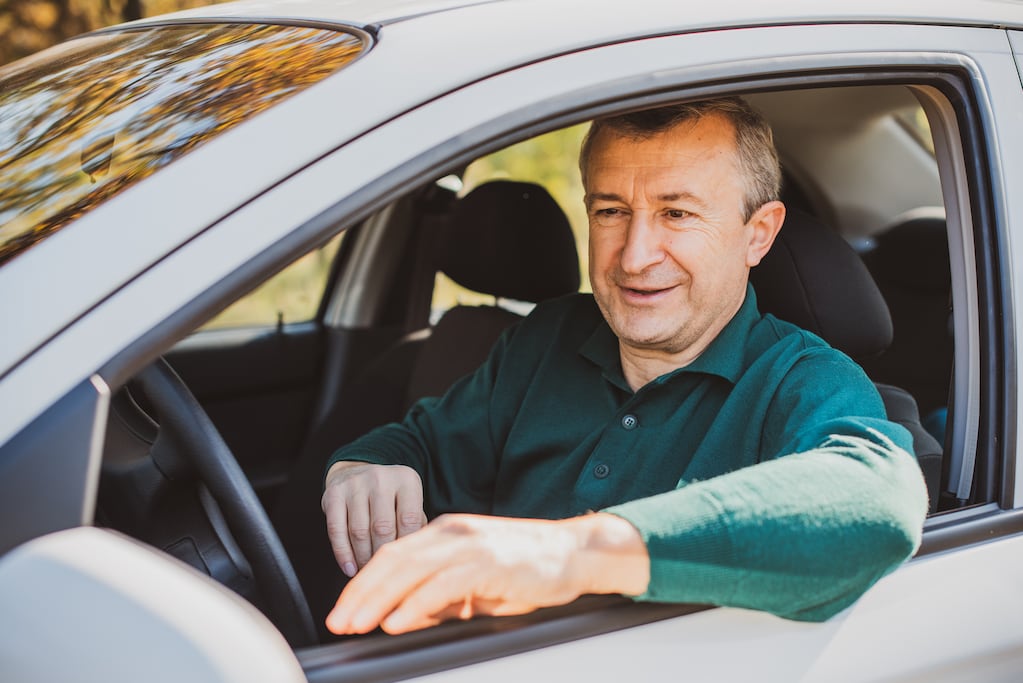 Hombre mayor sentado en el asiento del conductor de un coche, sonriendo