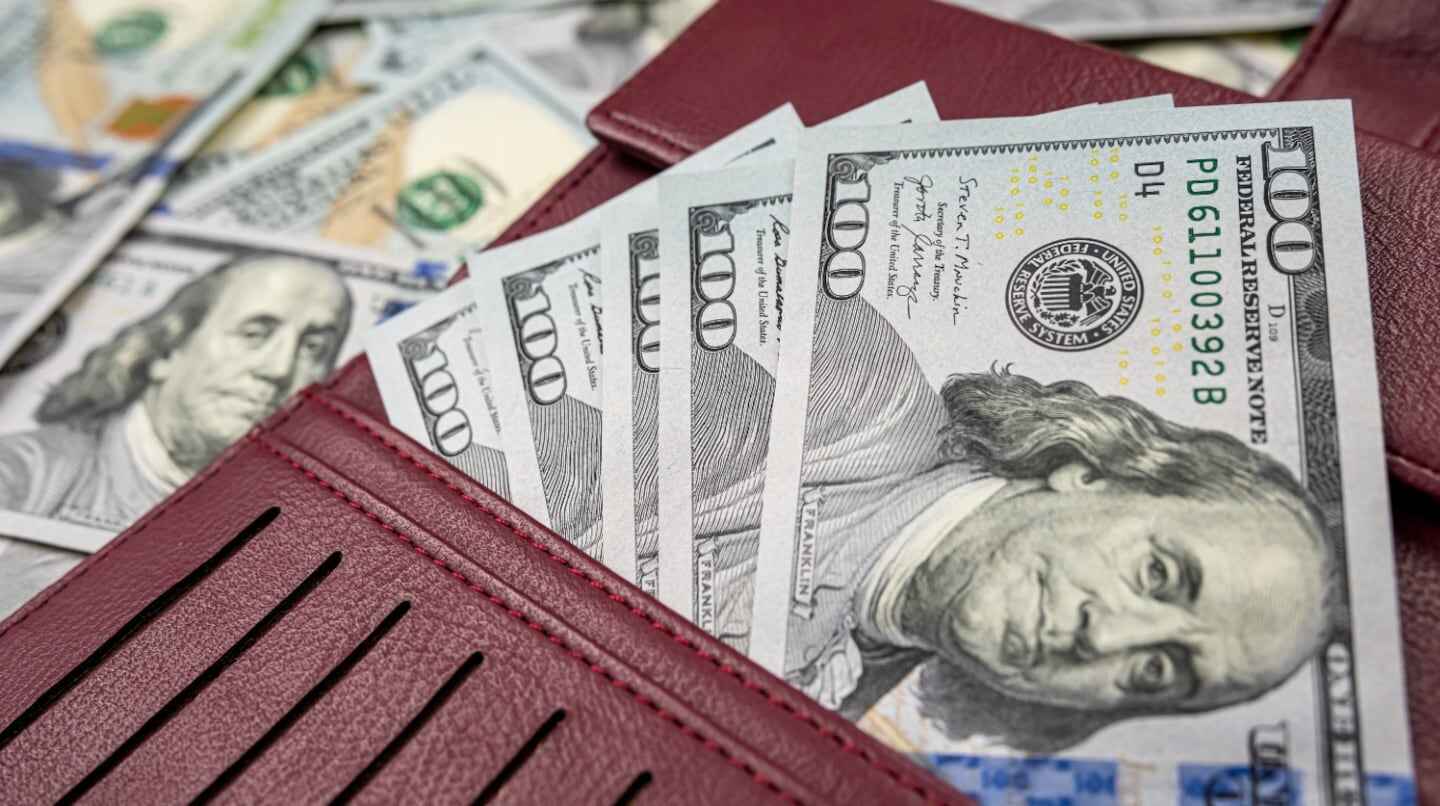 Billetes de 100 dólares en una billetera roja sobre un fondo de billetes