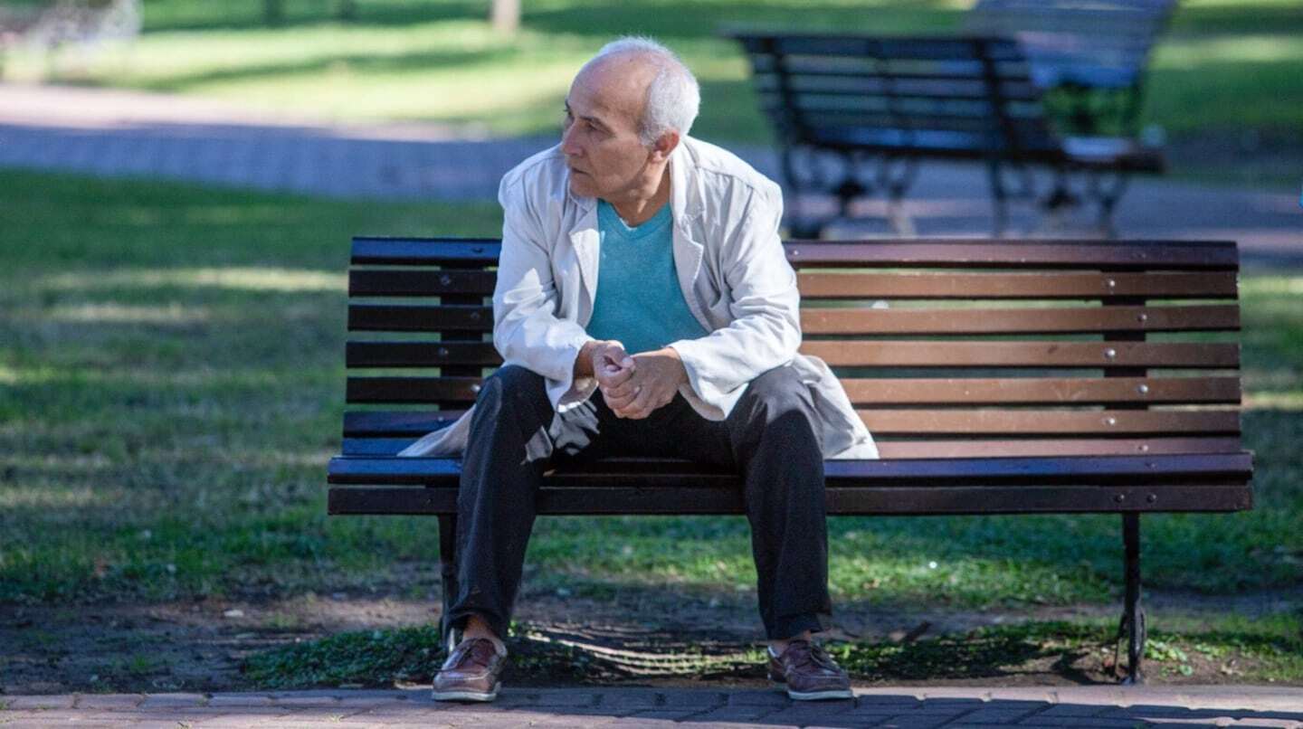 Hombre mayor sentado en un banco de parque, reflexionando sobre su situación financiera