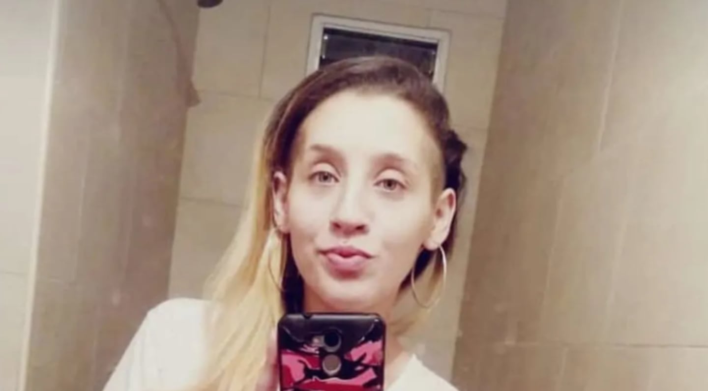 Mujer joven con cabello largo y rubio, sosteniendo un teléfono móvil en un espejo