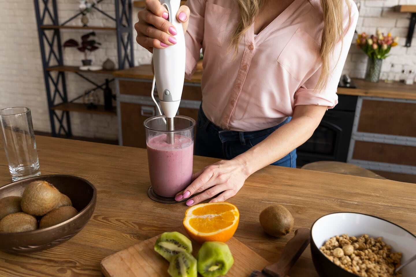 Mujer preparando un batido en la cocina con frutas y utensilios de cocina