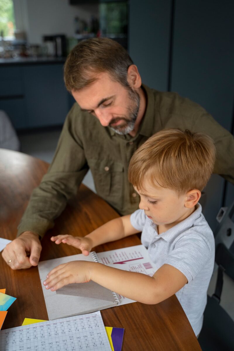 Padre e hijo interactuando en una mesa mientras revisan un libro