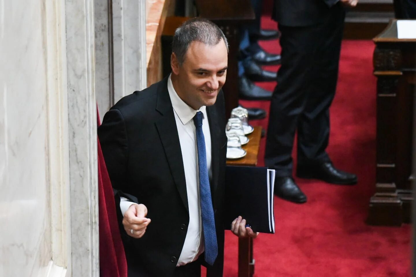Manuel Adorni saliendo del recinto legislativo con una carpeta en la mano