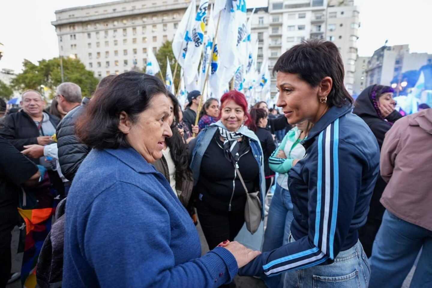 Dos mujeres conversan en un evento político en Lomas de Zamora, rodeadas de banderas