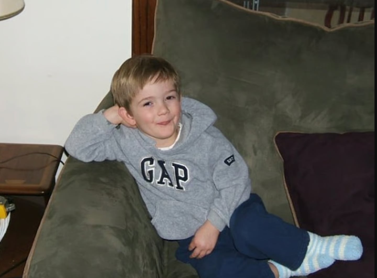 Timmothy Pitzen, un niño pequeño sentado en un sofá, con una sudadera gris y pantalones oscuros