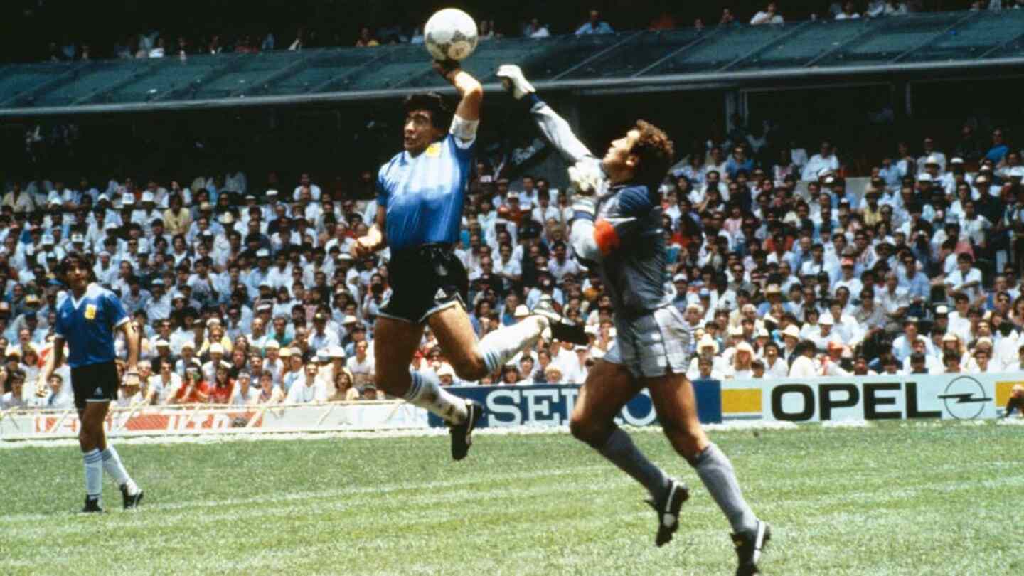 Diego Maradona en un partido de fútbol, saltando para interceptar el balón con un portero en el fondo