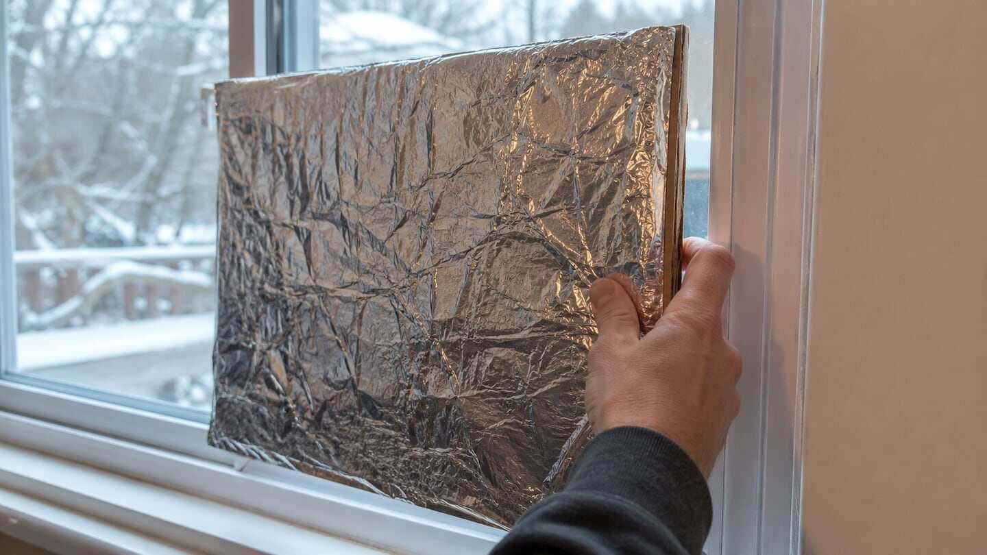 Persona colocando papel aluminio en una ventana para aislar el frío