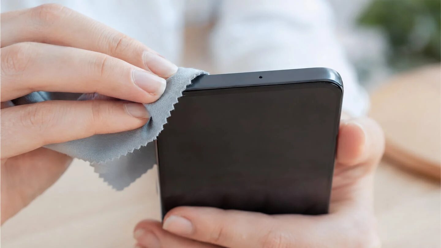 Persona limpiando la parte superior de un smartphone donde se encuentra el micrófono secundario