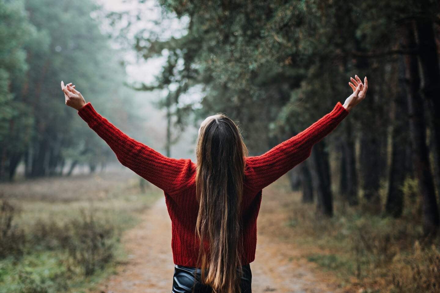 Mujer de espaldas con brazos extendidos en un bosque, simbolizando esfuerzo y libertad