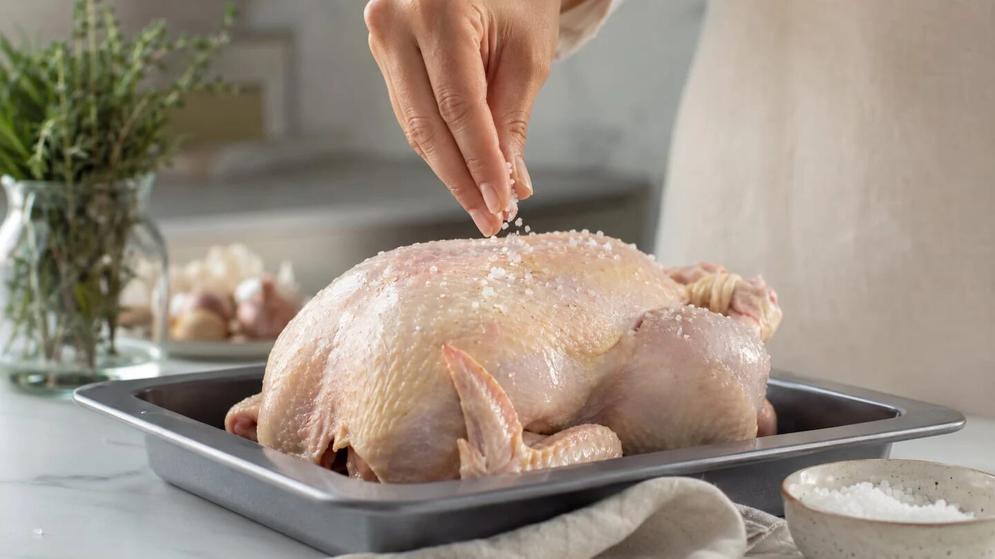 Chef espanol salando un pollo crudo en una bandeja para hornear