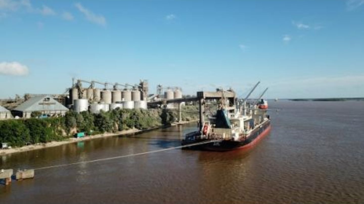 Barco de carga en la hidrovía con instalaciones agroindustriales al fondo