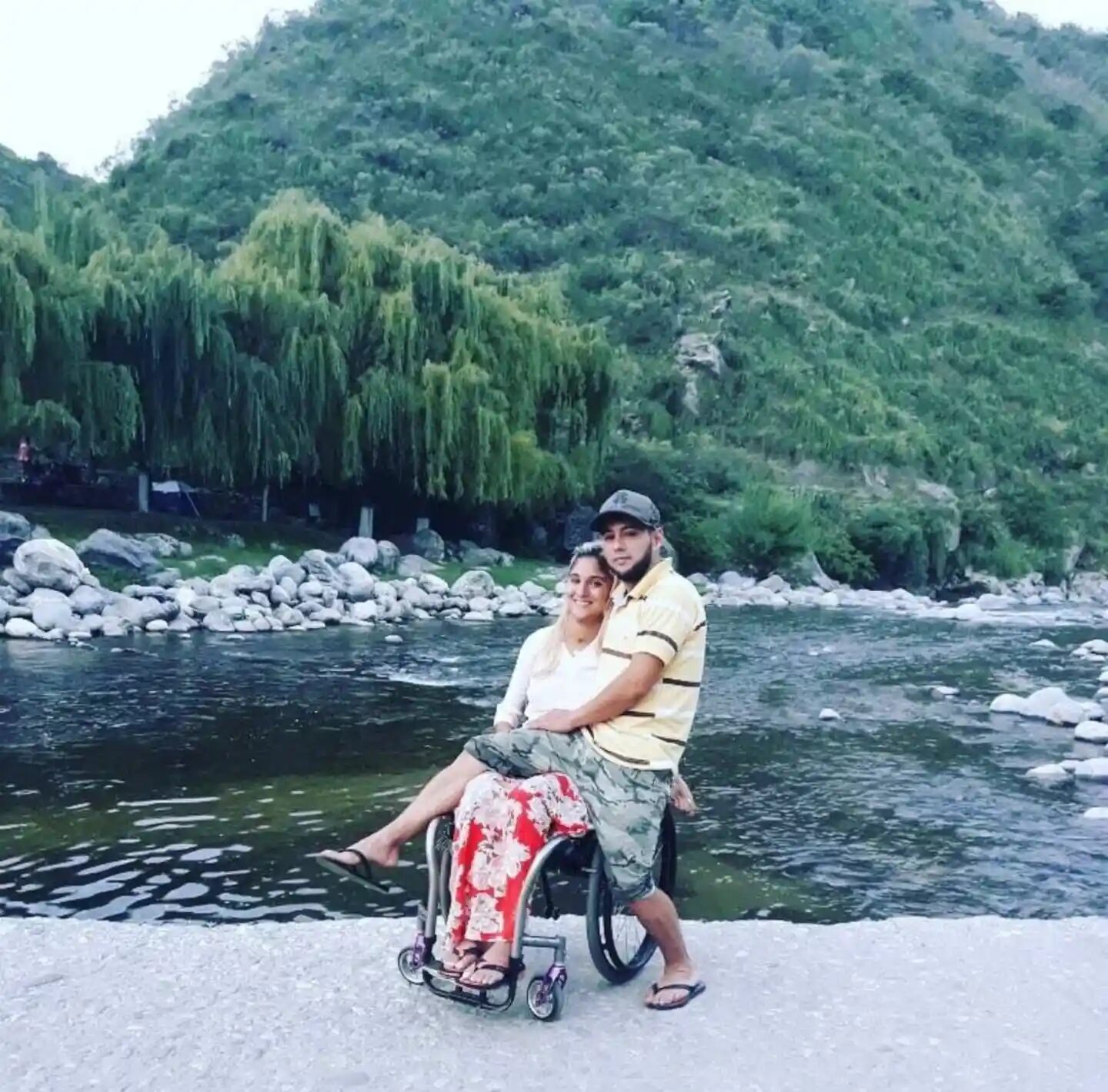 Giselle Agostino en silla de ruedas junto a un acompañante junto a un río
