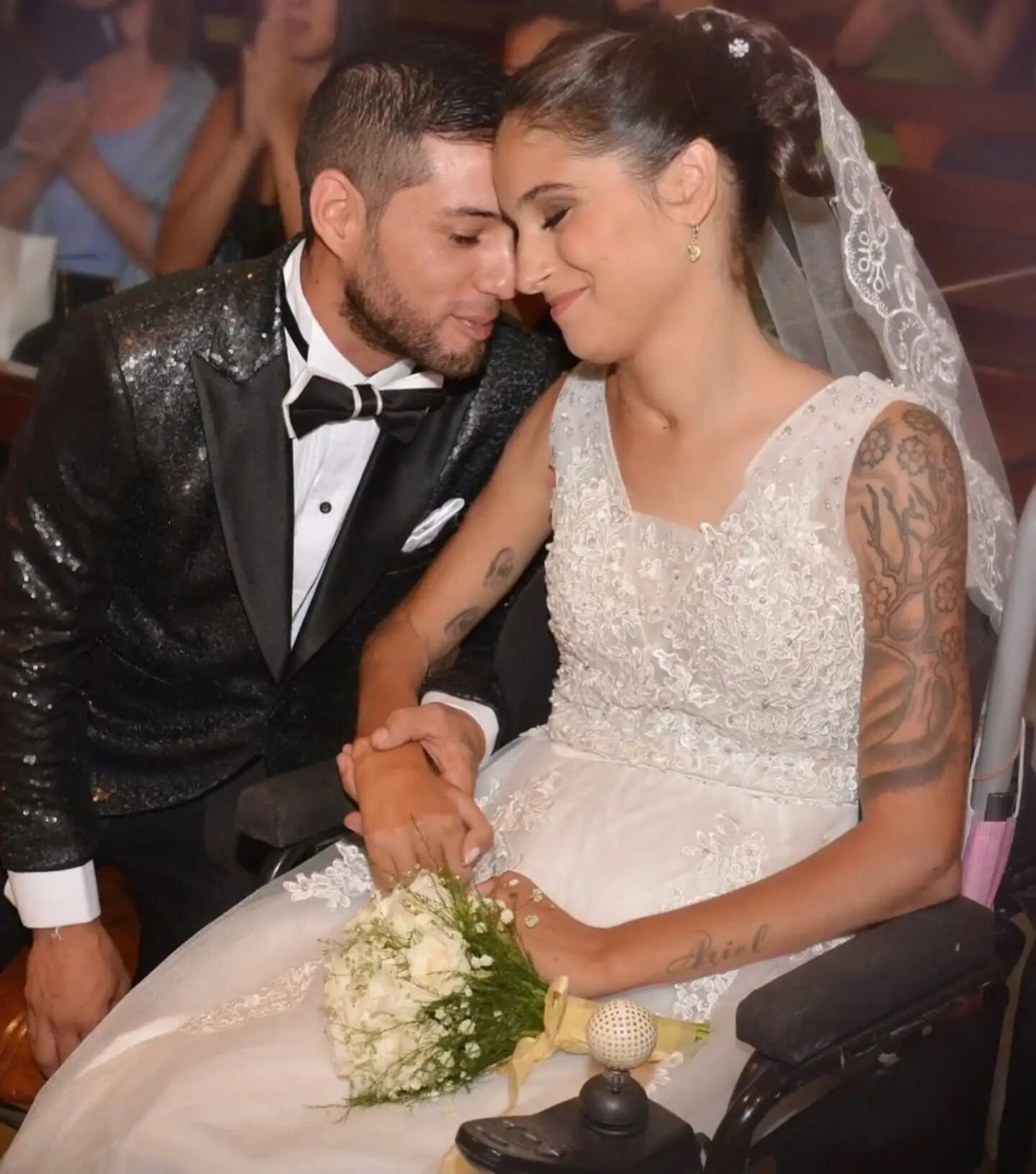 Giselle Agostino en su boda, sonriendo mientras sostiene la mano de su esposo desde una silla de ruedas