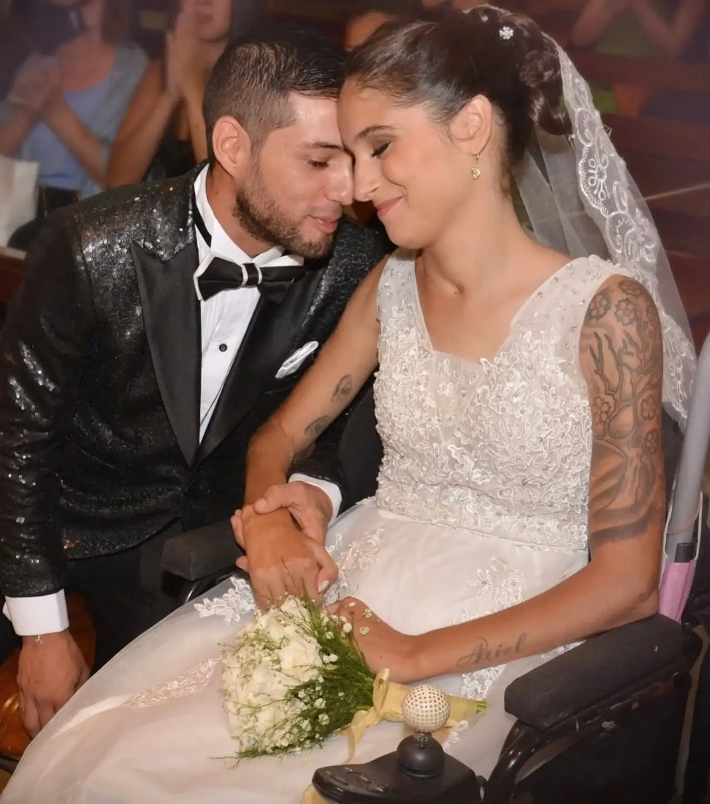 Giselle Agostino en su boda, sonriendo mientras sostiene la mano de su esposo desde una silla de ruedas