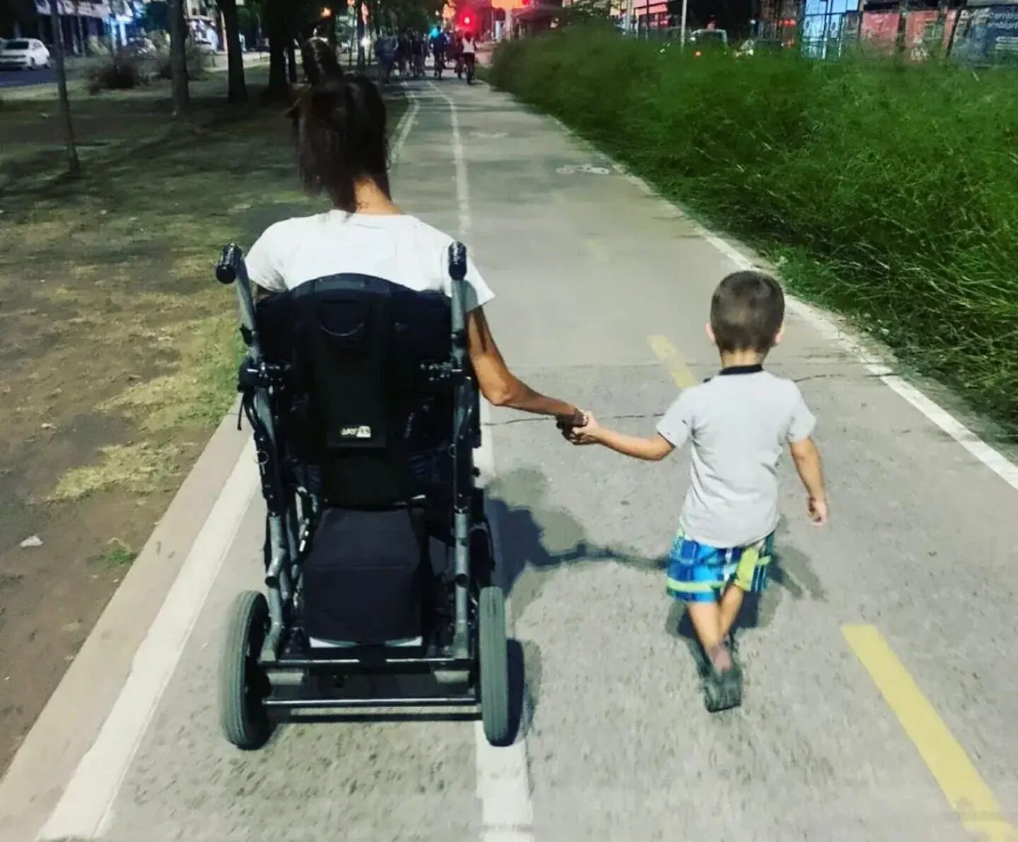 Giselle Agostino en silla de ruedas, caminando por un sendero junto a un niño que le toma la mano