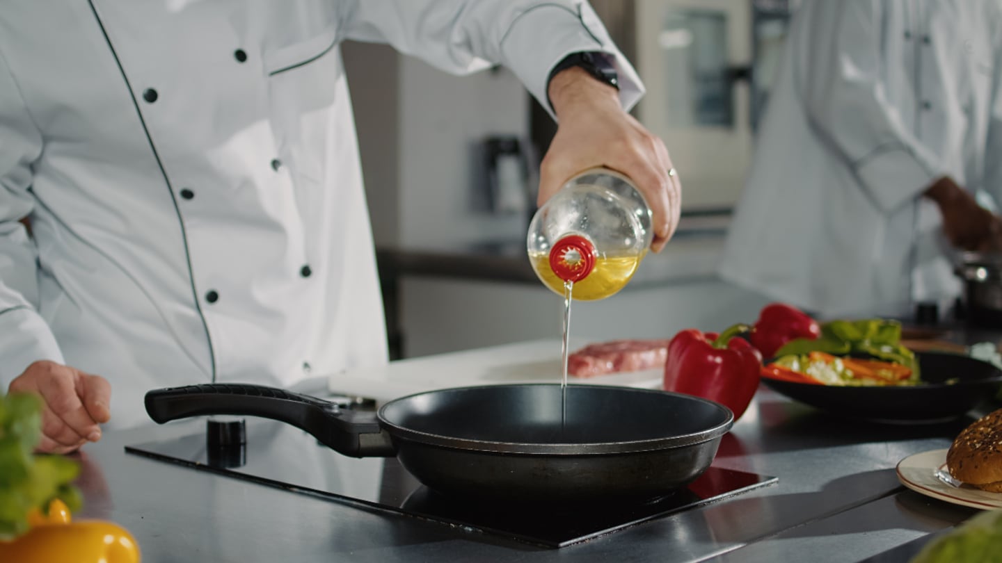 Chef vertiendo vinagre en una sartén para cocinar pollo