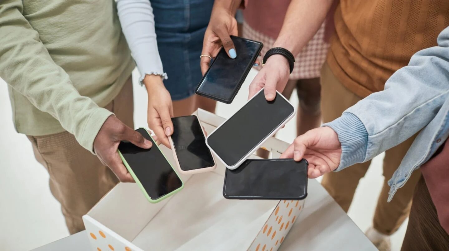 Varios estudiantes sosteniendo celulares sobre una caja en un entorno escolar
