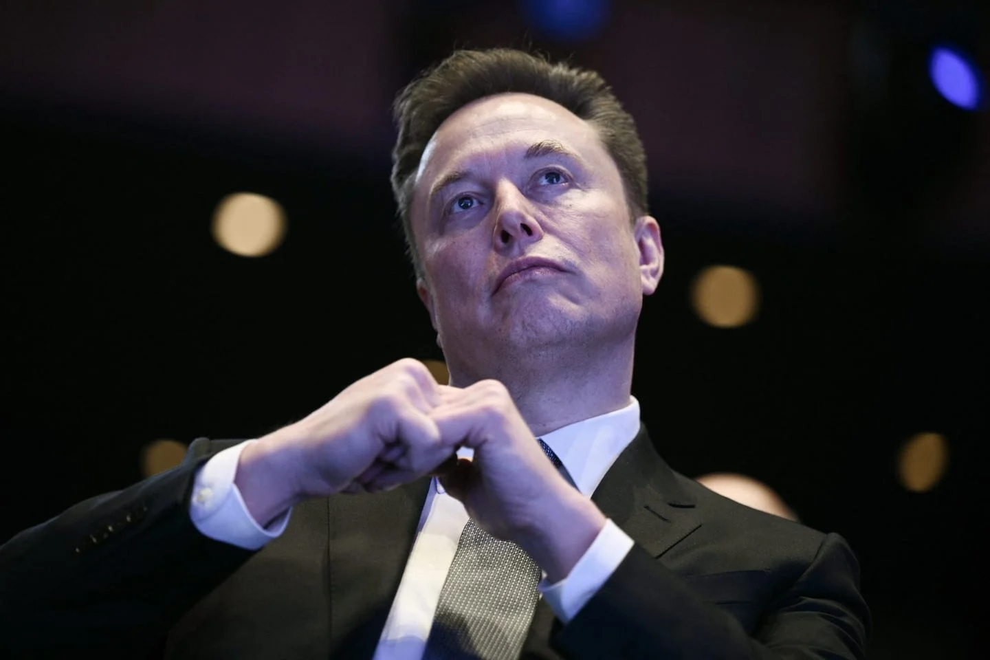 Elon Musk en un evento, con expresión pensativa y vestido formal