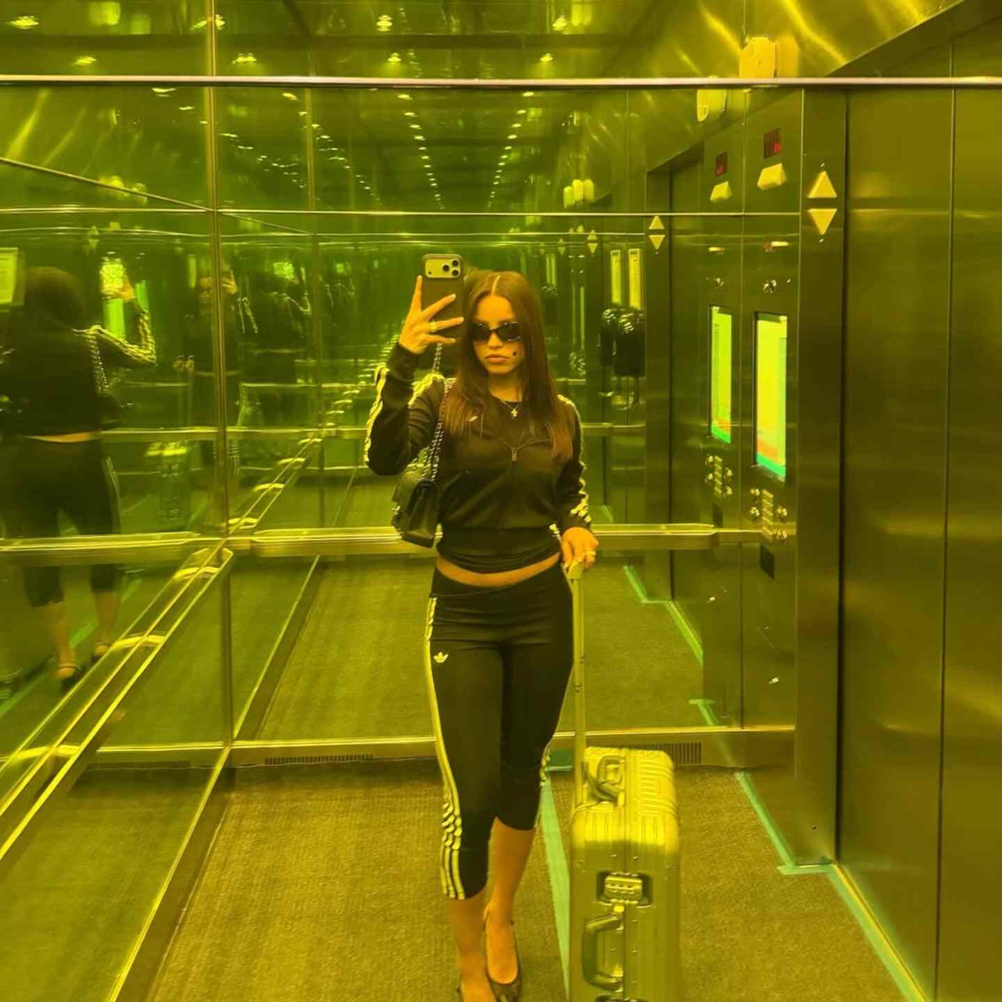 Emilia Mernes posando en un ascensor con un atuendo deportivo y maleta