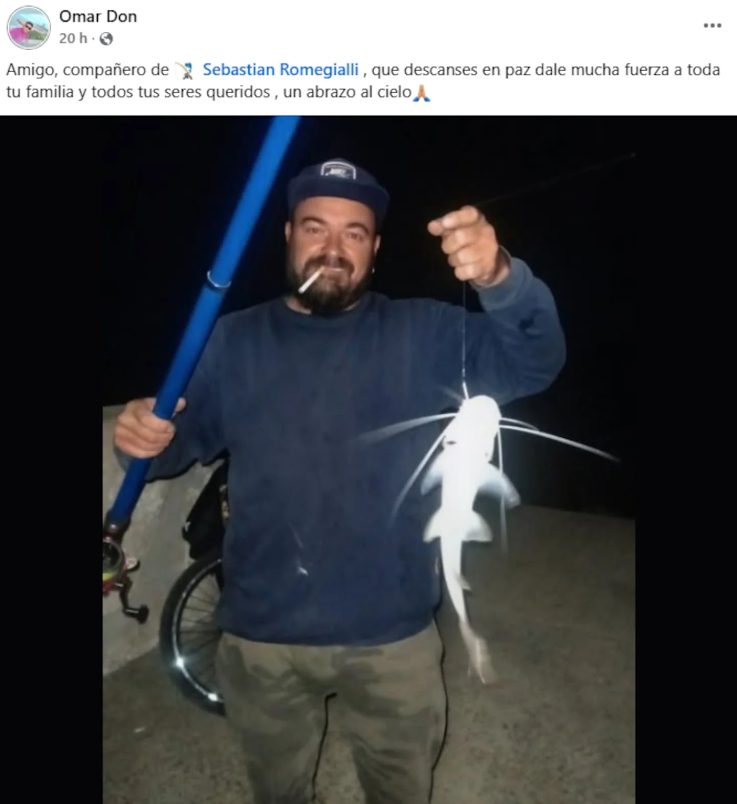 Hombre sosteniendo un pez mientras fuma un cigarrillo en la noche