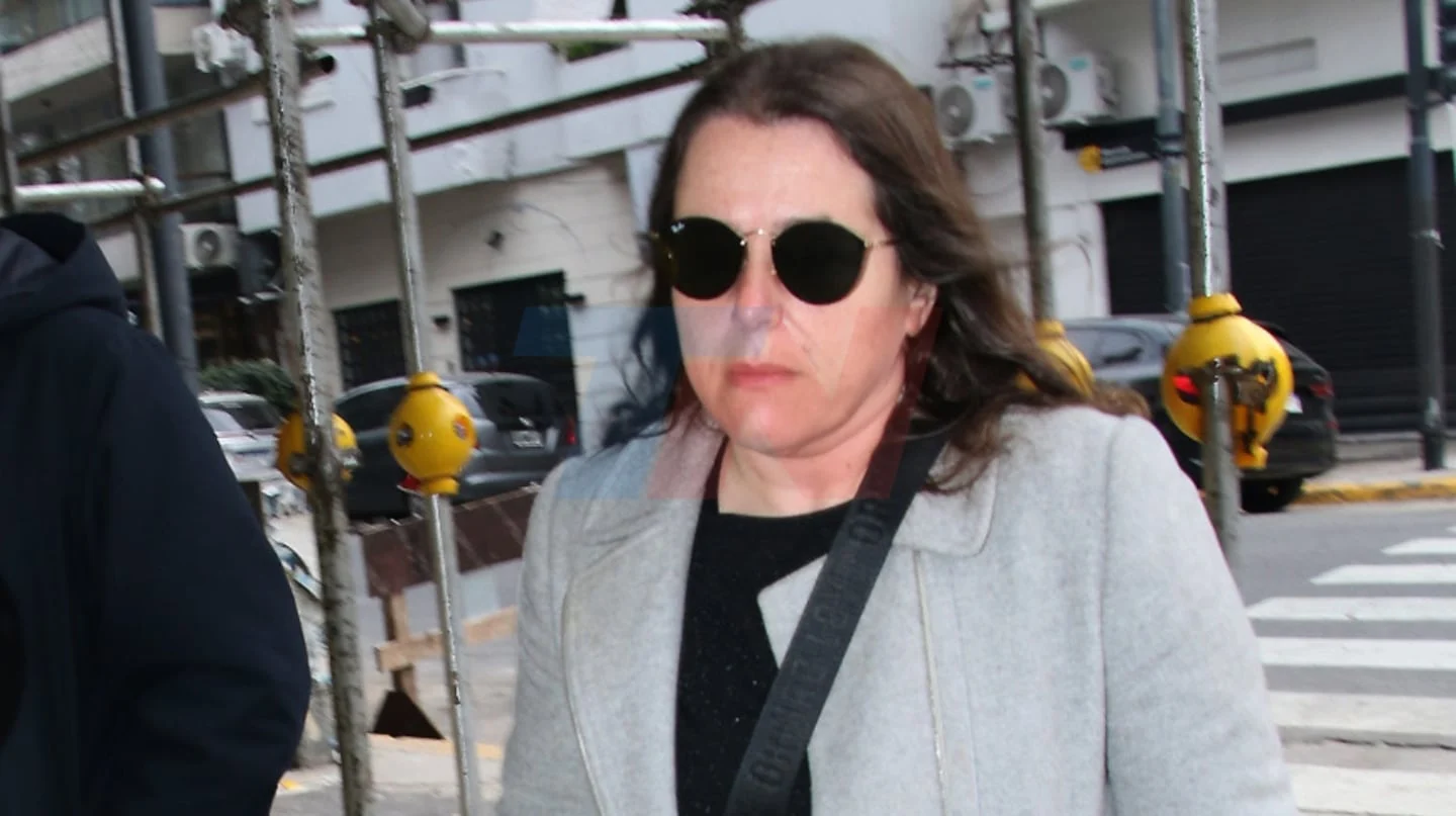 Mujer con gafas de sol y abrigo claro camina en un entorno urbano