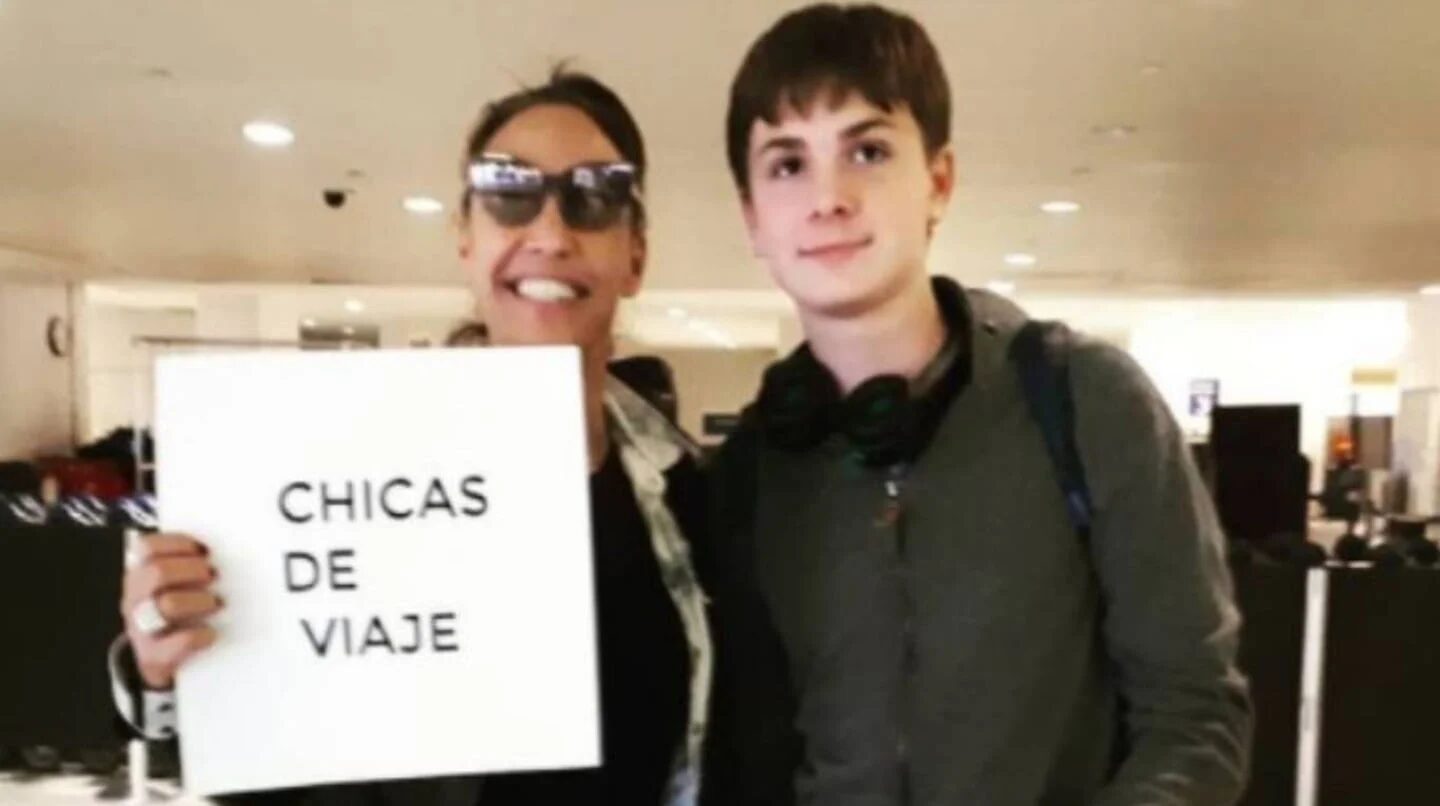 Benicio Guyot Pais junto a su madre, Ernestina Pais, sosteniendo un cartel que dice 'Chicas de viaje'