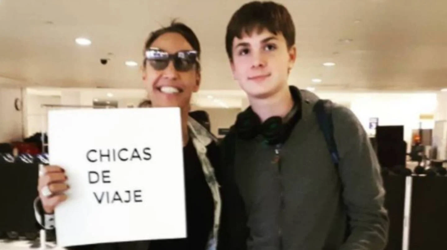 Benicio Guyot Pais junto a su madre, Ernestina Pais, sosteniendo un cartel que dice 'Chicas de viaje'